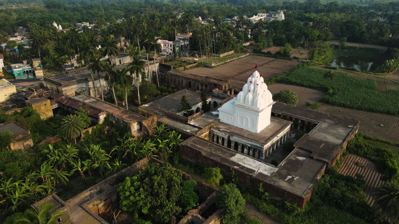 una toma aérea de un templo blanco bellamente diseñado, rodeado de exuberante vegetación y una atmósfera tranquila.