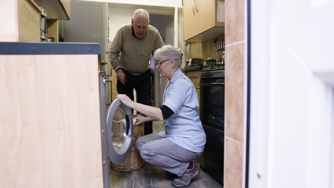 Caretaker helping senior man with washing machine in kitchen
