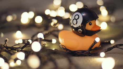 fotografía en primer plano de un pato de goma con un casco de motocicleta hecho a mano sobre el fondo de una guirnalda de navidad