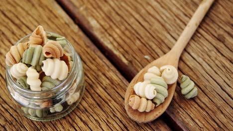 Colored-half-shell-shaped-pasta-in-jar-and-spoon-on-wooden-background