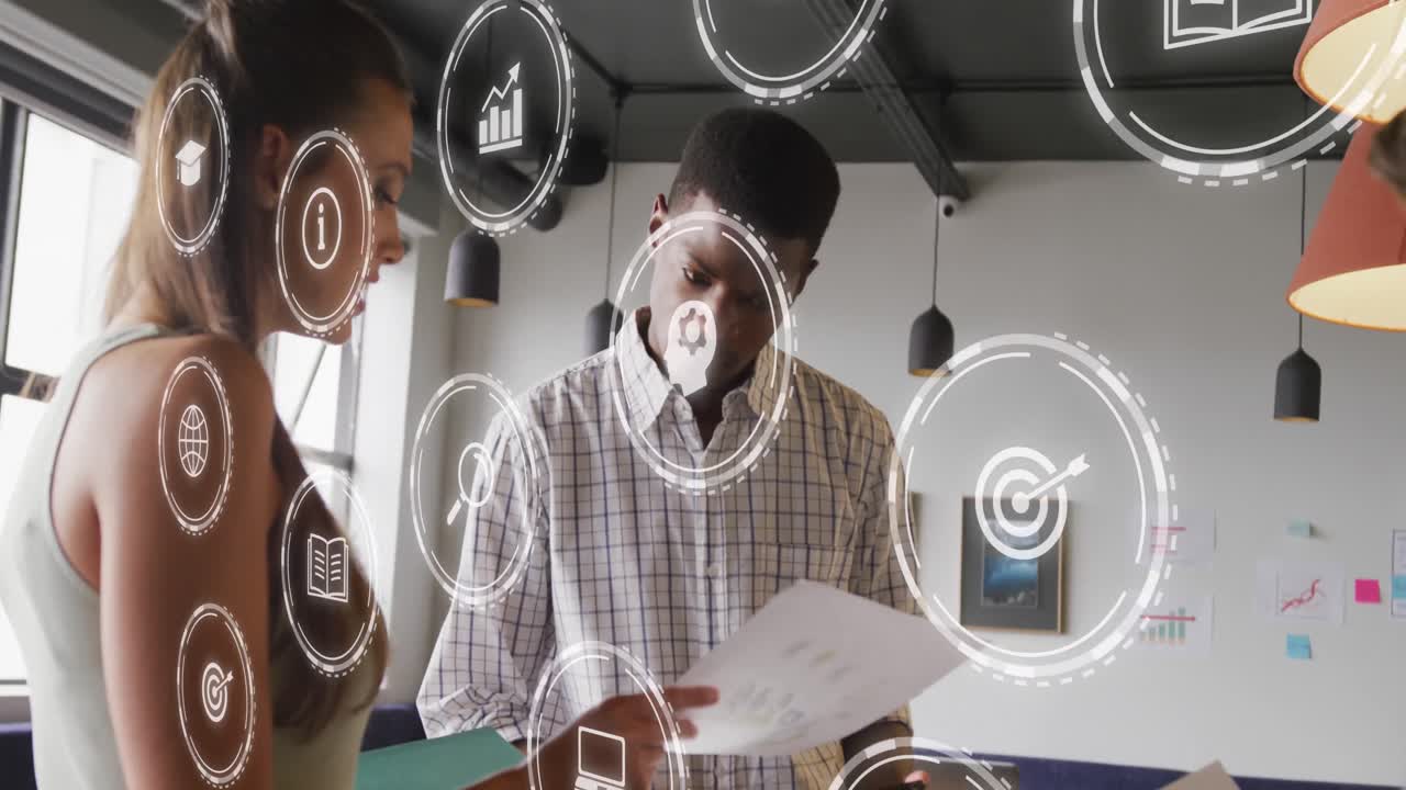 Animation of digital icons against diverse man and woman discussing over a document at office