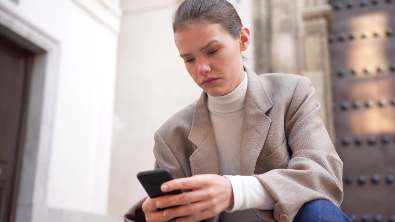 A contemplative young woman engaged with her smartphone while surrounded by an urban setting