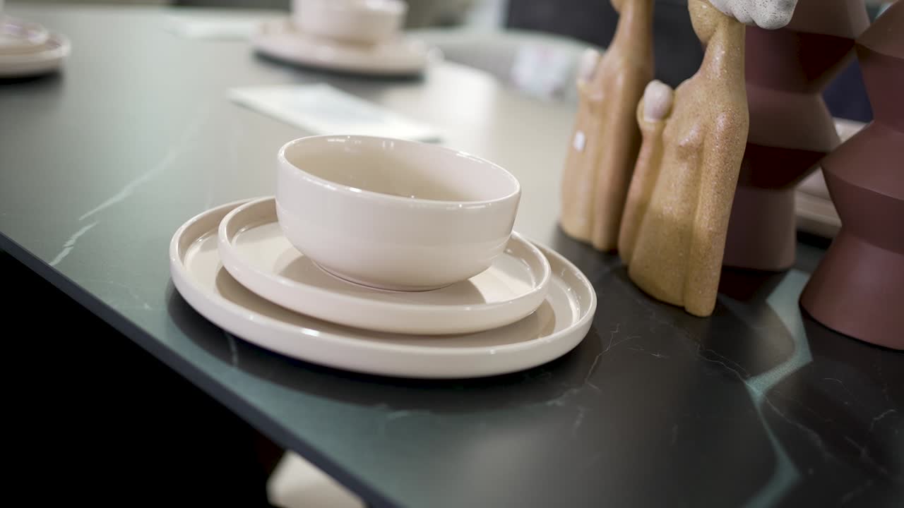 A minimalist dining arrangement showcases elegant ceramic dishes, plates, and decorative figures on a stylish black table, reflecting contemporary design trends