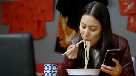 mujer comiendo fideos mientras usa teléfono móvil 4k