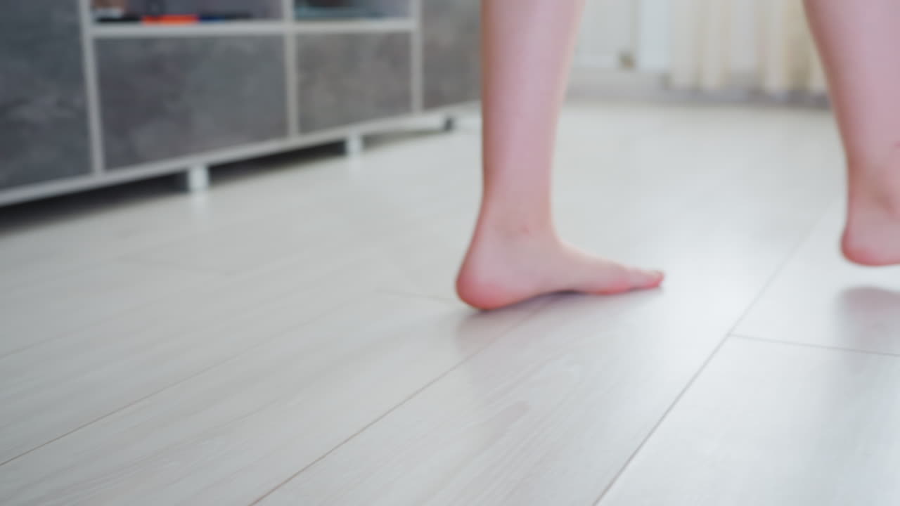 Close up leg view of woman walking across light wood floor inside modern living space barefoot steps showing calf and foot movement towards sofa area near doorway in bright minimalist interior