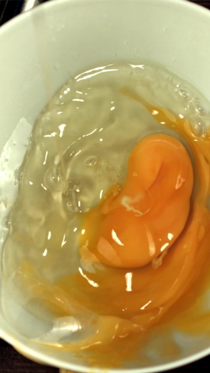 Raw Egg Yolk and White Falling into a White Bowl