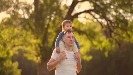 Un-Padre-Amoroso-Sonríe-Caminando-Con-El-Niño-Sentado-En-El-Cuello-Al-Atardecer-En-Un-Prado-En-Verano-En-Cámara-Lenta.