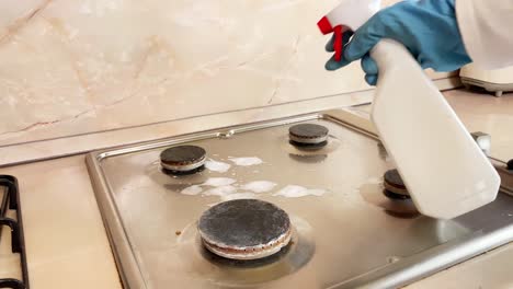 hand in blue glove polishes gas stove in the kitchen, cleaning gas hob