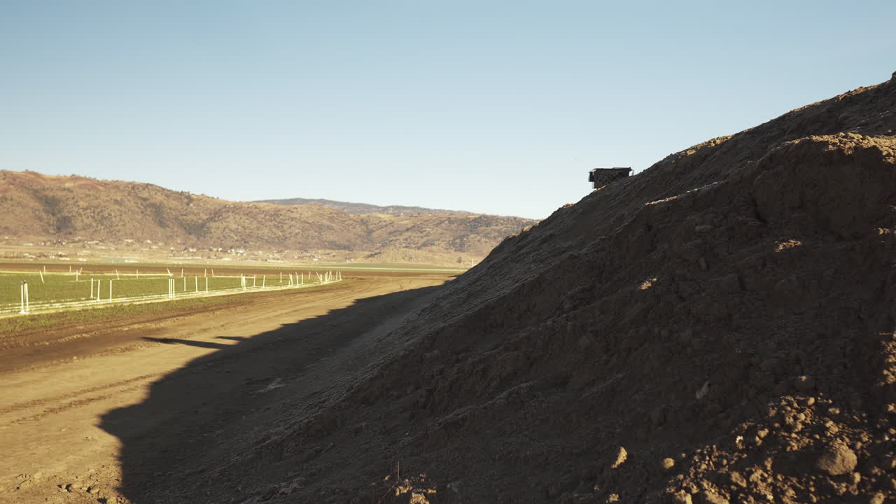 plano general de un hombre en una colina de tierra instalando un equipo junto a un campo agrícola para ayudar a entrenar halcones y halcones para proteger los campos agrícolas de las plagas de aves
