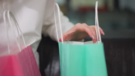 close-up of a hand with polished nails gracefully opening a mint-colored shopping bag while seated, the vibrant green and pink bags enhance the stylish shopping scene