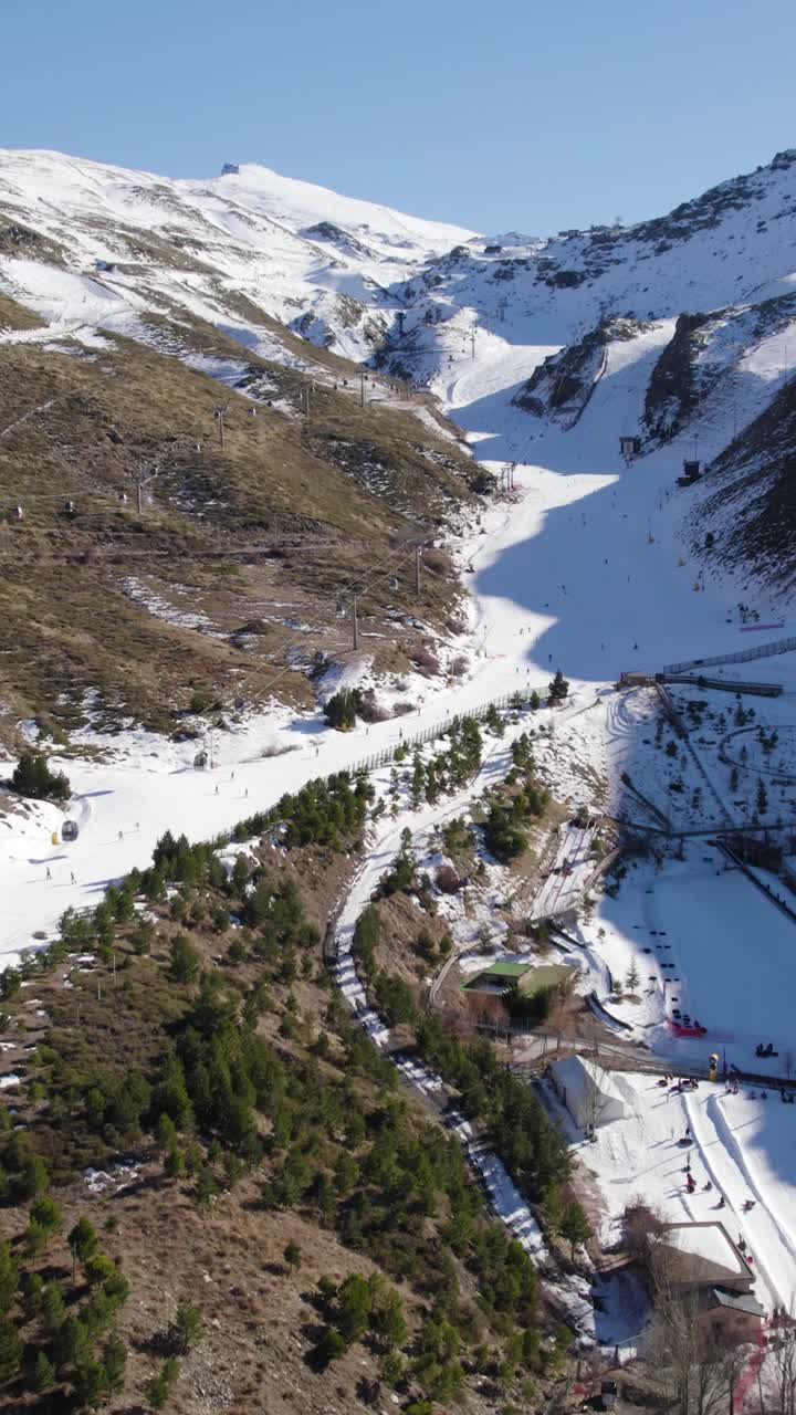 Vertikal flygbild med drönare som fångar människor som åker skidor nedför snöiga backar på Sierra Nevadas skidort i Spanien