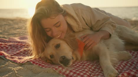 close-up shot: a blonde girl and her cute big dog of light coloring lie side by side on a mat on a sunny beach in the morning. happy time with your pet