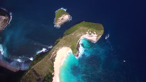 drone flying down above kelingking beach on nusa penida island over the seashore green peninsula yellow sand