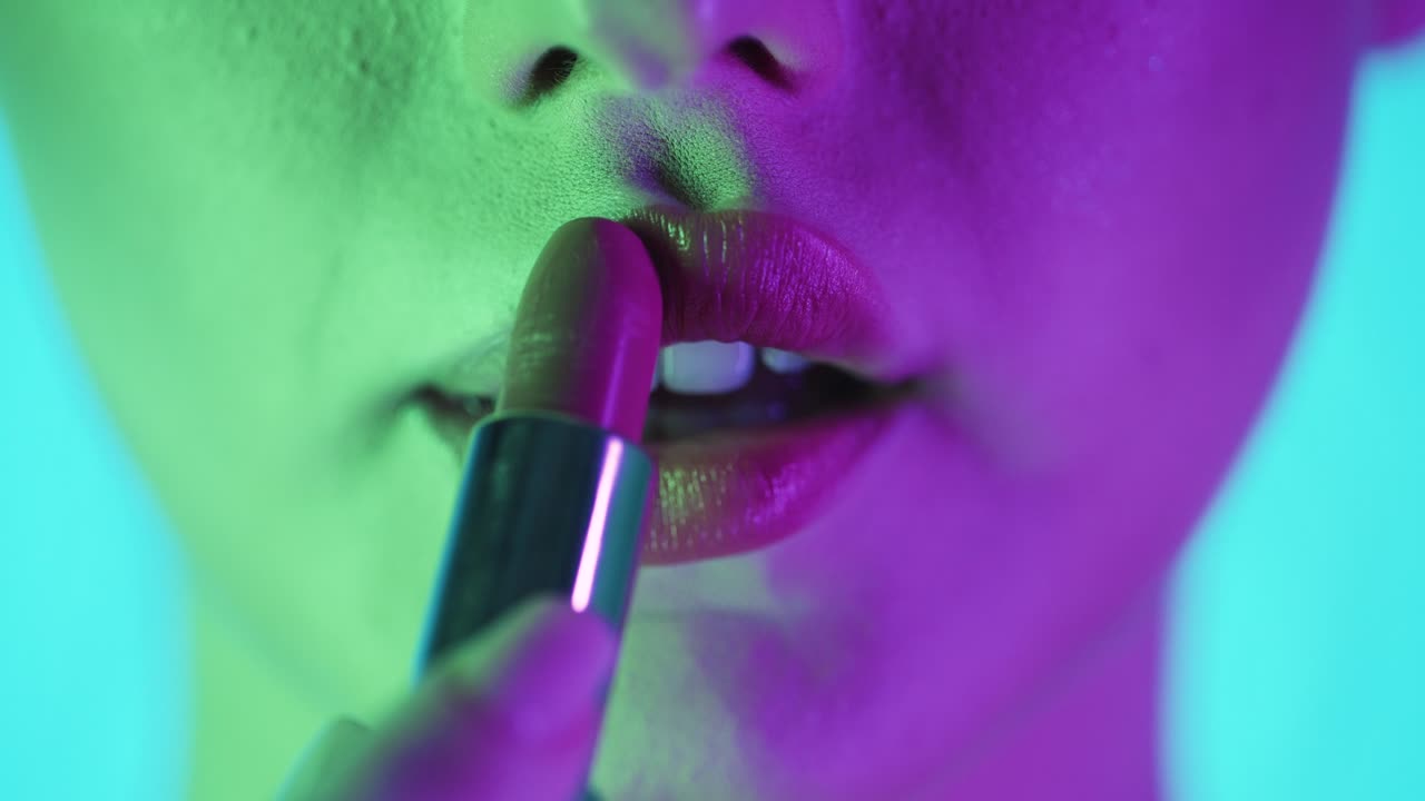 acercamiento extremo de los labios de una hermosa mujer llena mientras se aplica lápiz labial rojo y se prepara para la noche o la cita con contraste púrpura verde en su cara