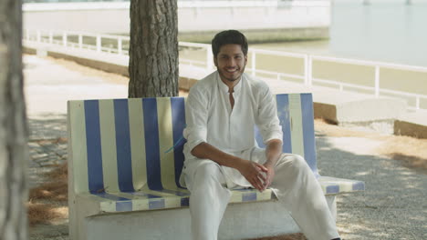 happy young muslim man sitting on bench at river bank.