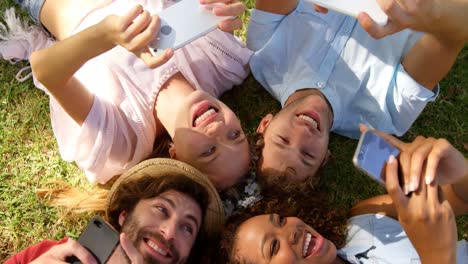 a group of  hipster friends lying head to head and watching their smartphone