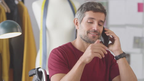 Reifer-Männlicher-Modedesigner-Im-Rollstuhl-Im-Studio,-Der-Mit-Dem-Mobiltelefon-Spricht