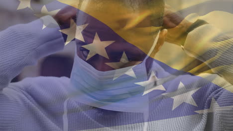 animation of waving bosnia and herzegovina over african american man wearing face mask on the street