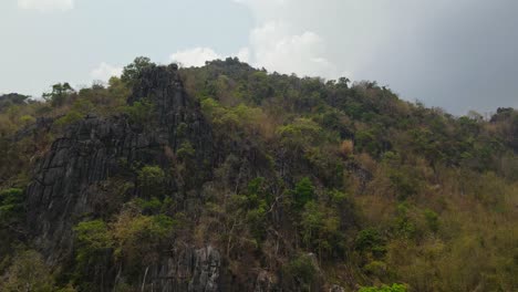 4k-Luftfahrtaufnahme-Einer-Wunderschönen-Kalksteinfelsenklippe,-Die-Mit-üppigem-Grünen-Wald-Bedeckt-Ist,-Der-In-Der-Bergkette-In-Thailand-Südostasien-Gefunden-Wurde