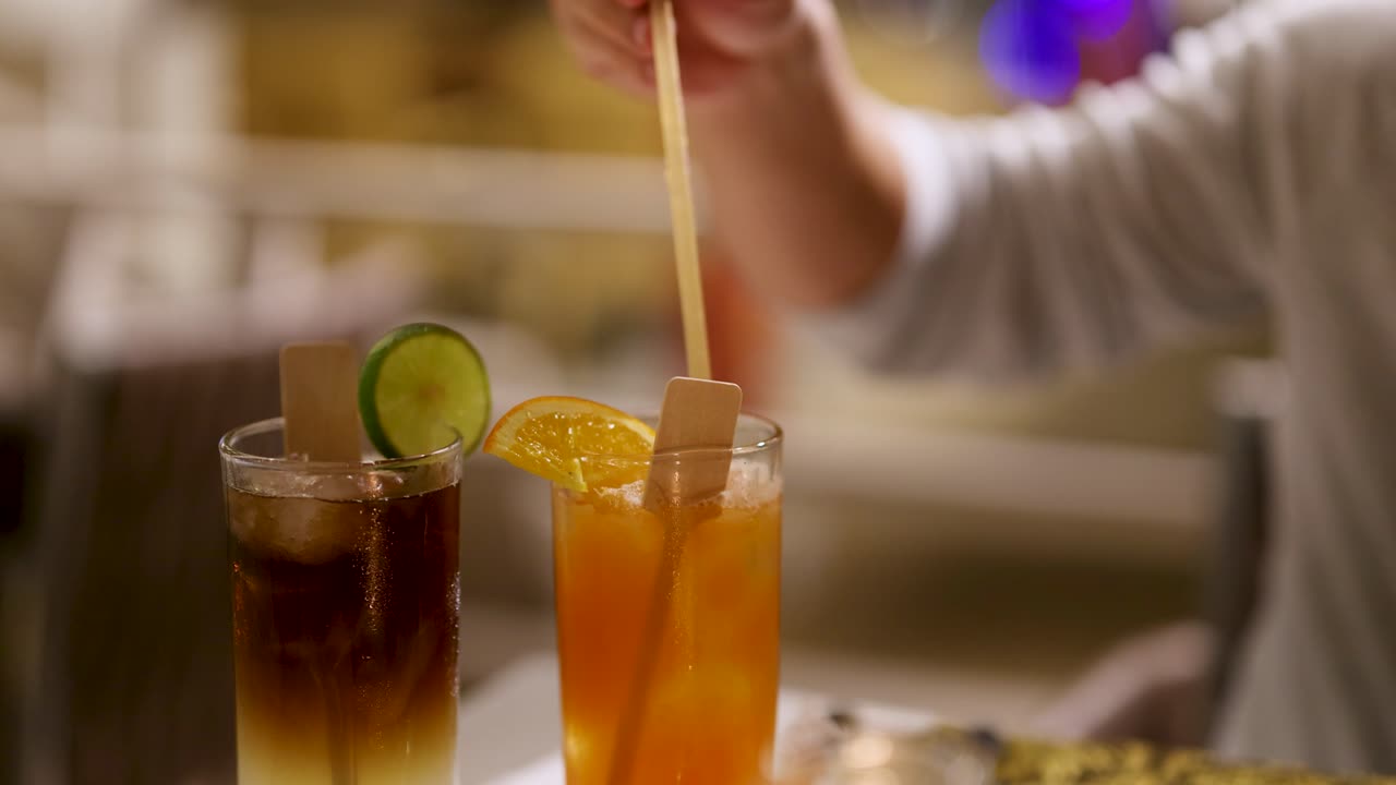 바텐더가 뜨거운 불빛으로 빛나는 술집에서 사탕수수 장식으로 두 개의 테일을 는다.