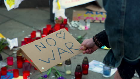 Placing an antiwar sign between candles and Ukraine flags on pavement