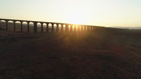 low aerial drone shot rising towards silhouetted ribblehead viaduct train bridge at stunning sunrise in summer in yorkshire dales england uk