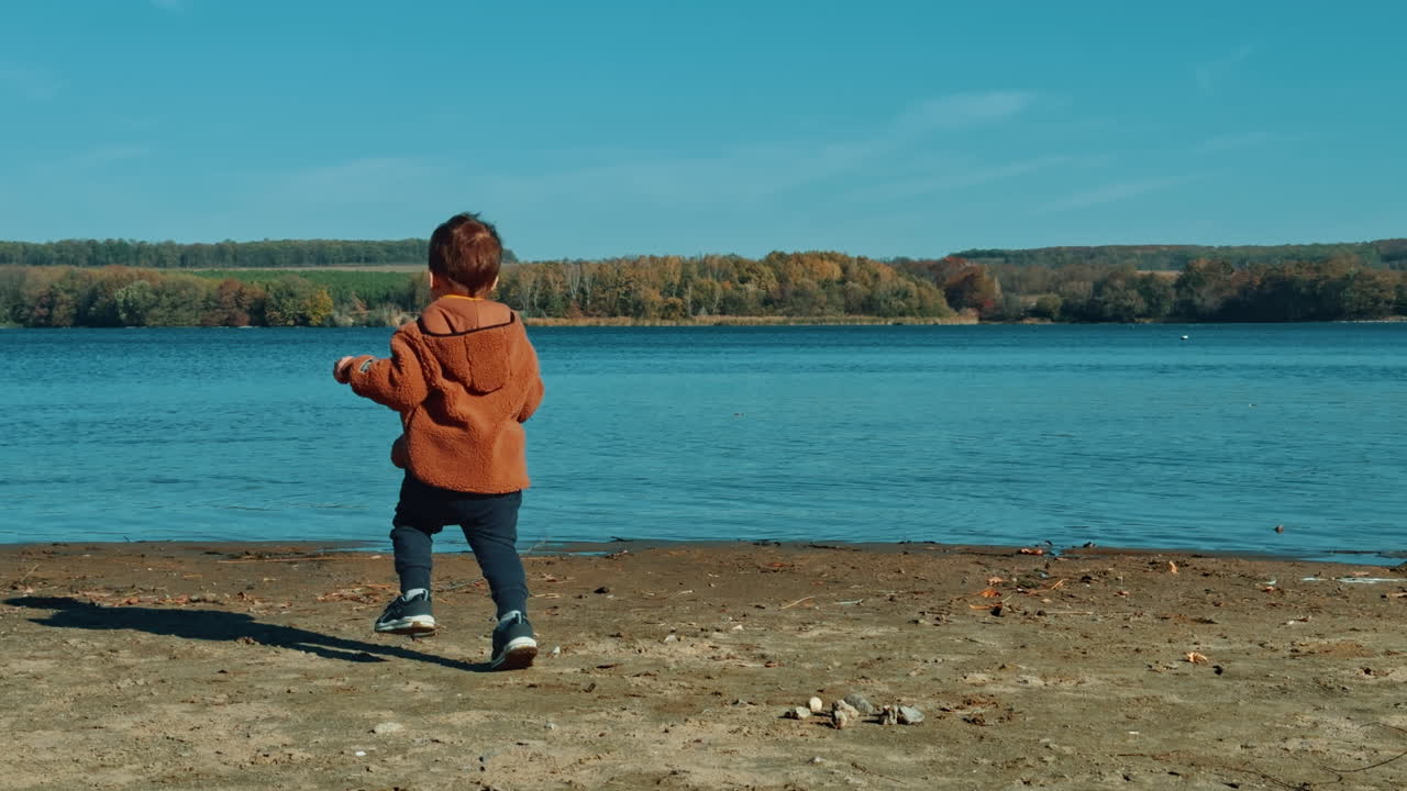 Excited toddler throwing stones into the river. Baby boy spending time in the nature in autumn.