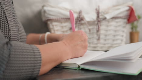 close up of hand flipping page and writing on other side in notebook with ash color basket and blurred potted flower in background under soft natural light