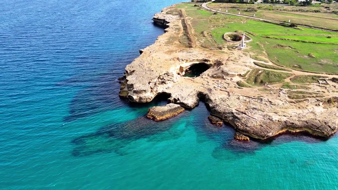 Ripresa aerea con drone che si allontana rivelando la Grotta della Poesia, grotte calcaree naturali, formazioni costiere rocciose e acque turchesi cristalline a Roca Vecchia, Melendugno, Puglia, Italia