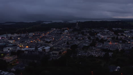 Aerial-panoramic-footage-of-evening-town-under-overcast-sky.-Lake-and-cloud-shrouded-hills-in-distance.-Killarney,-Ireland