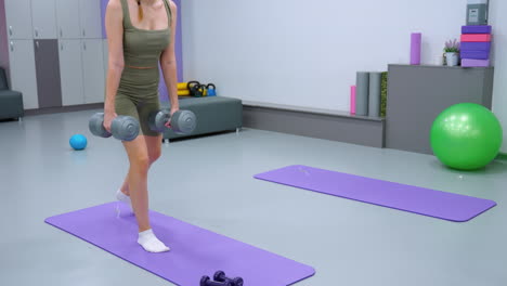 mujer centrada en ejercicios con pesas en una alfombra de yoga, realizando entrenamiento con pesos en una sala de fitness brillante, mantiene el equilibrio y la fuerza, rodeada de equipos de gimnasio y artículos esenciales para el ejercicio