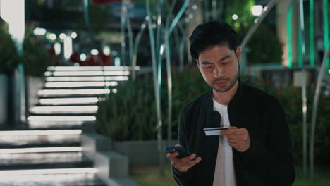 man using mobile phone and credit card for online payment in city at night