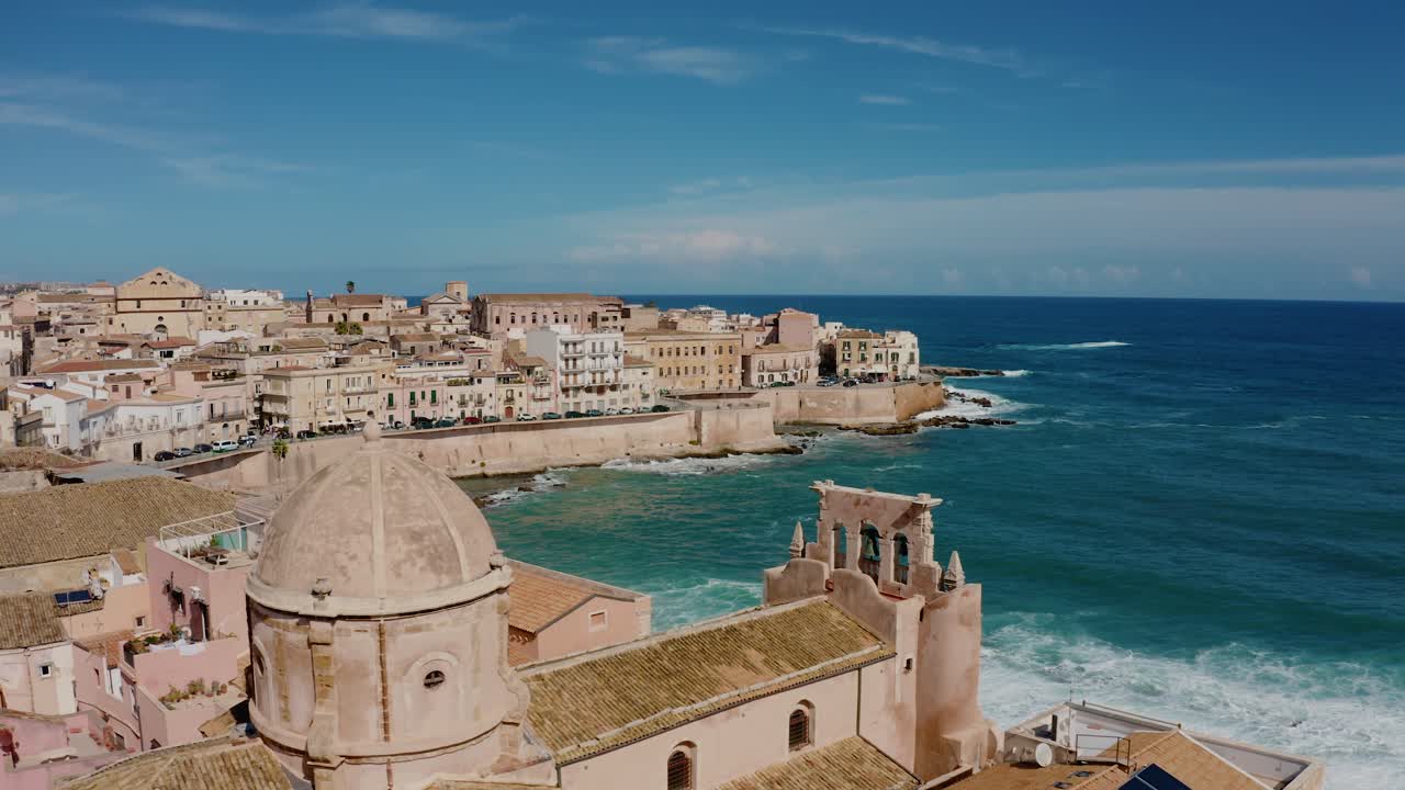 Flying around cathedral tower in Ortigia island. Chiesa dello Spirito Santo. Aerial drone shot of historic old town by the Mediterranean sea in Syracuse. UNESCO world heritage site in Sicily.