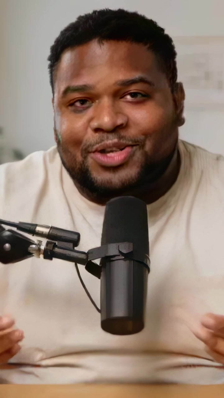 Vertical video: Speaking host gesturing mid-speech presenting in home studio in cream tee by mic