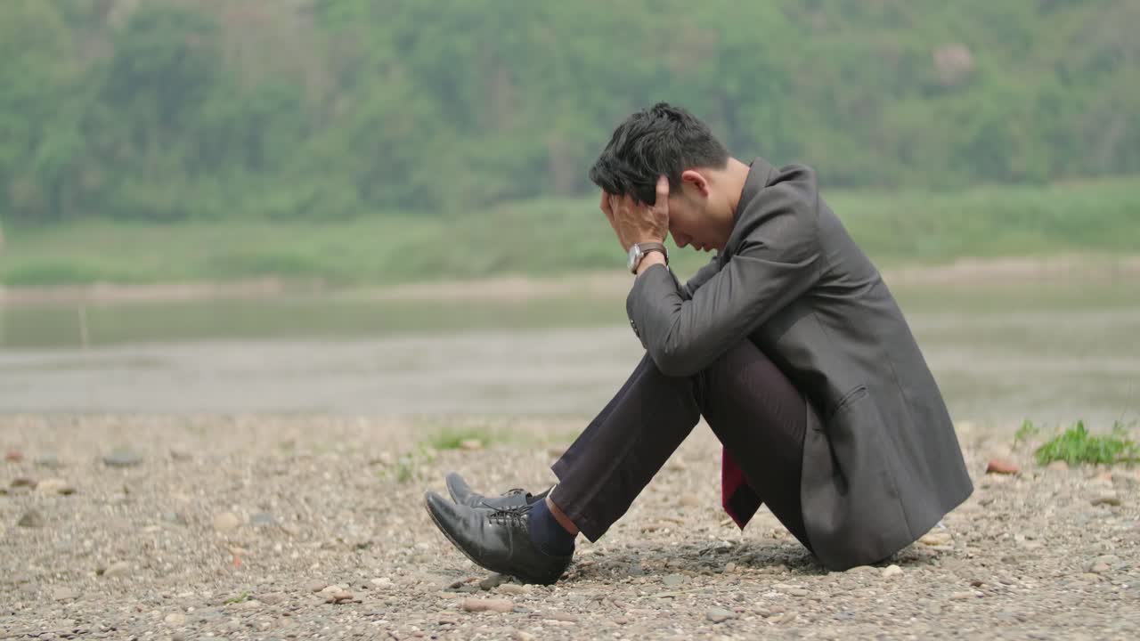 Depressed Businessman Sitting on a River Bank