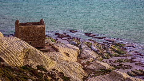 High-angle-shot-over-old-ruins-of-an-abandoned-tone-house-along-white-beach-on-cliff,-Punta-Bianca,-Agrigento-in-Sicily,-Italy