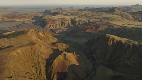 a wide aerial view of thakgil, iceland, revealing sprawling volcanic highlands, winding valleys, and streams under soft golden sunlight.
