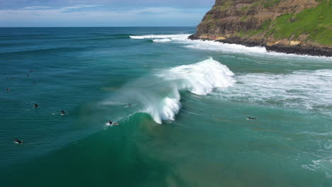 4k-Drone-shot-of-a-big-ocean-wave-next-to-some-people-surfing-in-Lennox-Head,-Australia