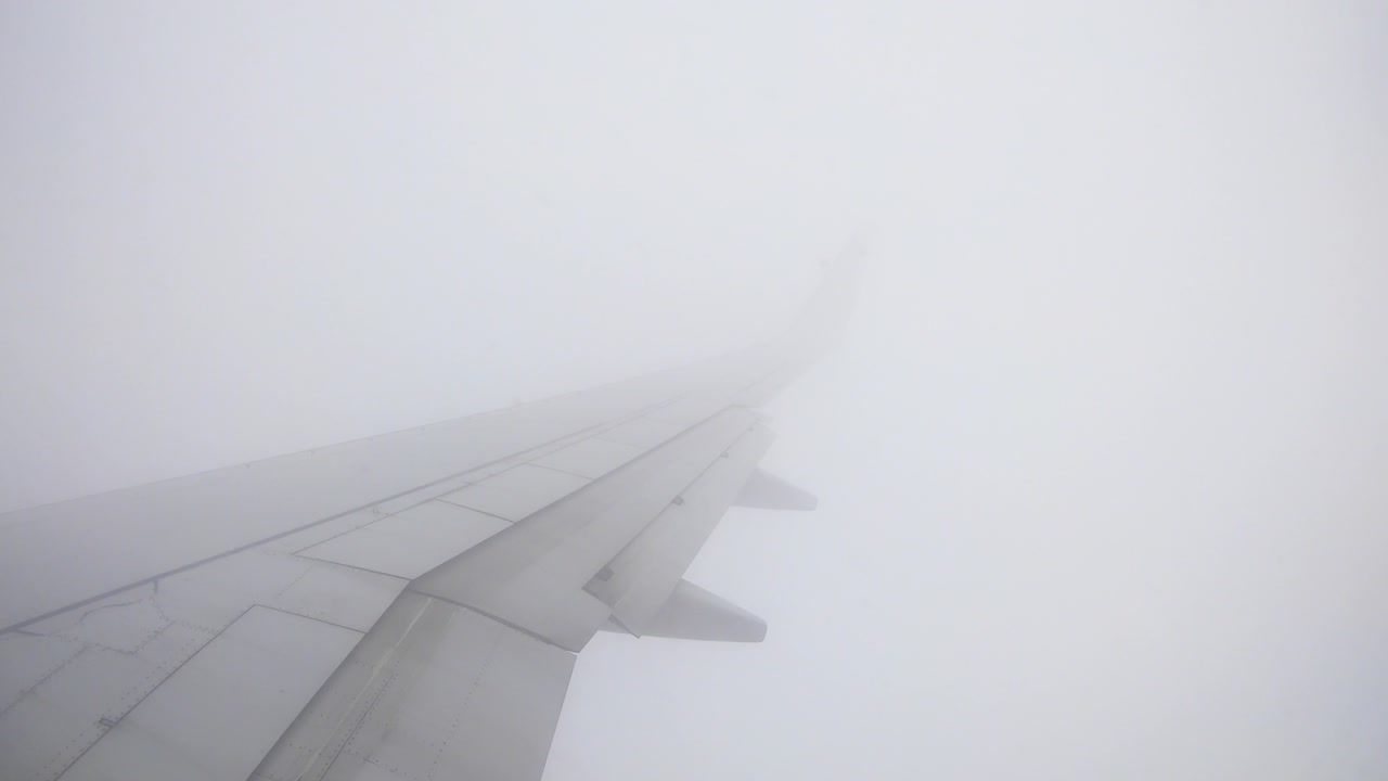 구름 사이의 난기류 지역을 통해 아래쪽에 도시 전망이 있는 맑은 하늘로 날아가는 창가 좌석 광각 날개 뷰 비행 장면