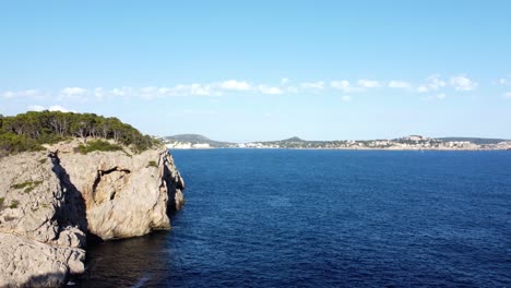 drone sitting stationary atop a cliff and then moving slowly towards the open ocean with the shoreline in view in mallorca spain