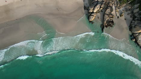 Wunderschöne-Türkisblaue-Meereswellen-Auf-Weißem-Sand-Am-Strand-Von-Llandudno-Mit-Großen-Felsbrocken,-Antenne-Von-Oben-Nach-Unten