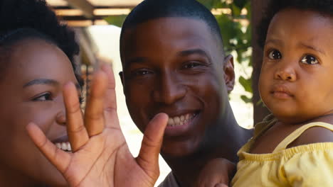 portrait of parents cuddling young daughter and waving outdoors at home