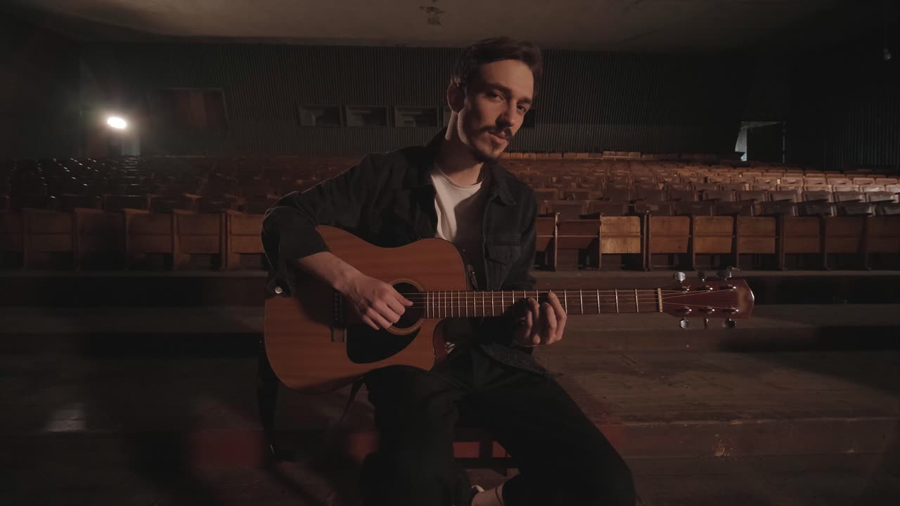 Un chico apuesto toca una guitarra acústica en un cine abandonado. El músico canta una canción y se acompaña con la guitarra