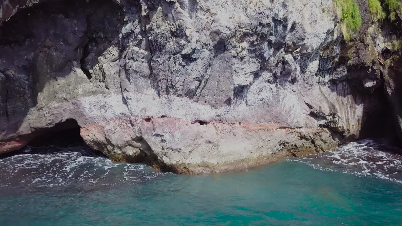 toma de drones de cuevas en acantilados junto al mar con olas rompiendo en las rocas.