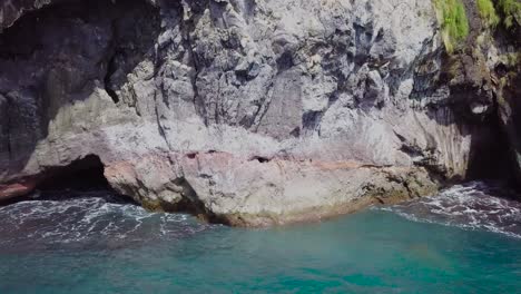 Drone-shot-of-seaside-cliff-caves-with-waves-lapping-at-rocks