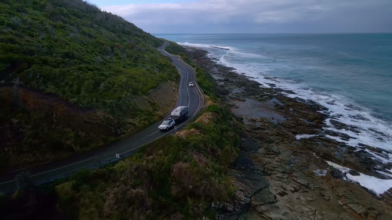 suv blanco con remolque de caravana conduce a lo largo de la esquina curva de la carretera del gran océano de australia en victoria