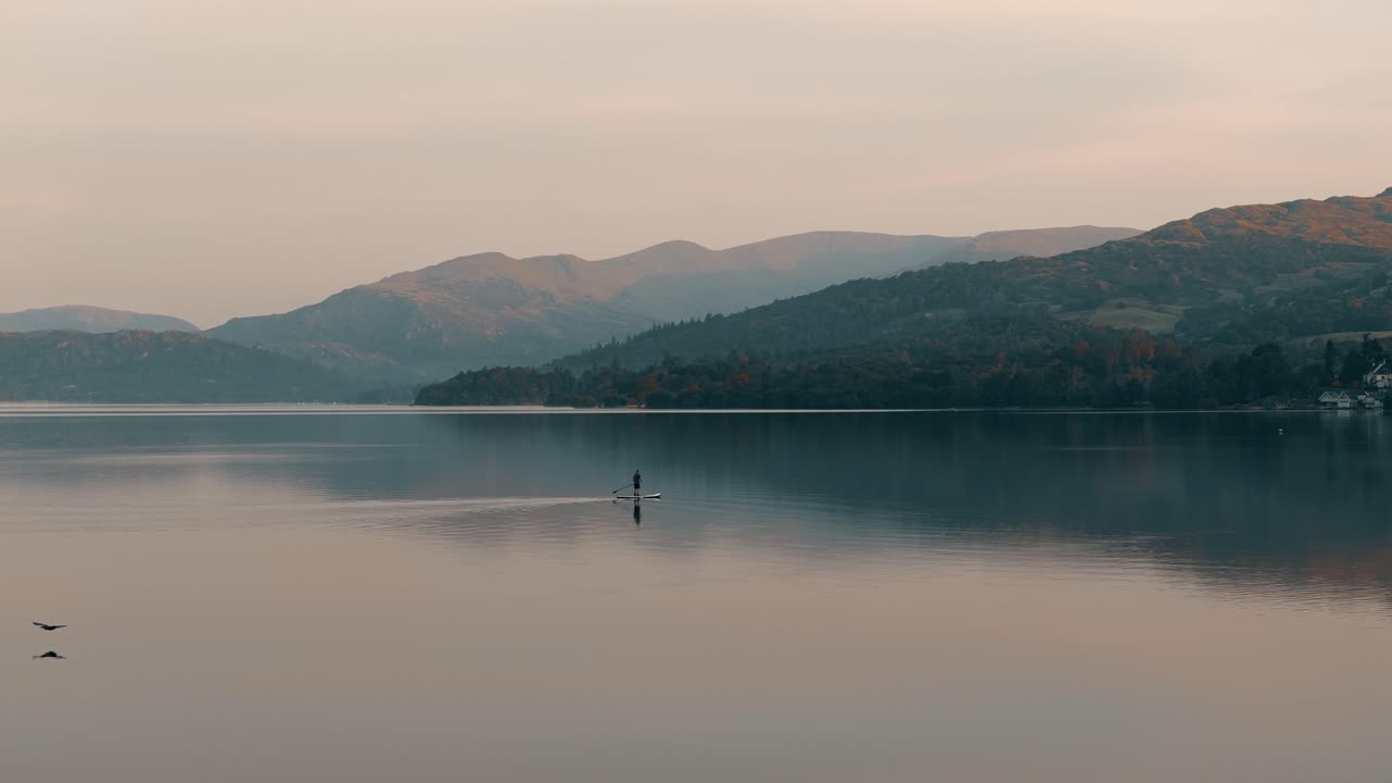 Stationary view of lone paddle boarder on calm Windermere Lake at sunrise