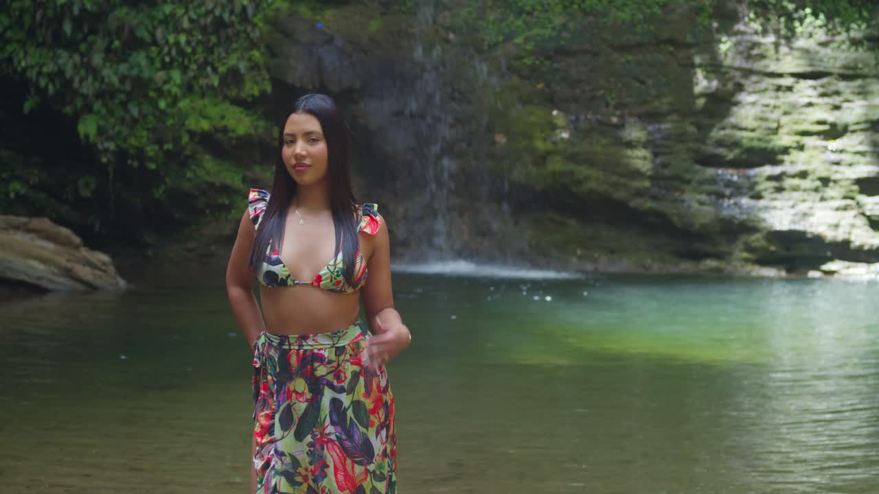 A woman in a bikini basking near a cascading waterfall in the Caribbean.