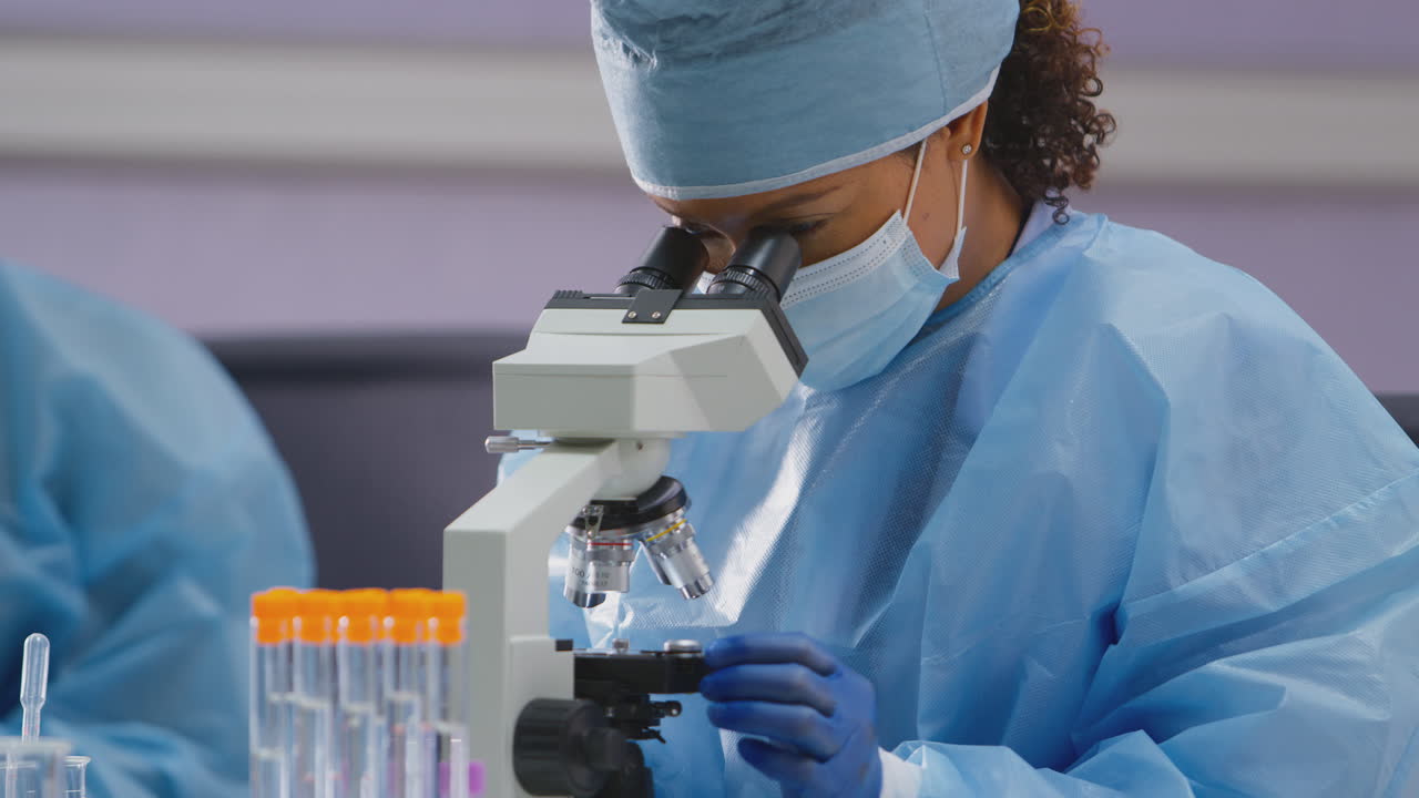 Female Lab Worker Wearing PPE Analysing Slide Under Microscope