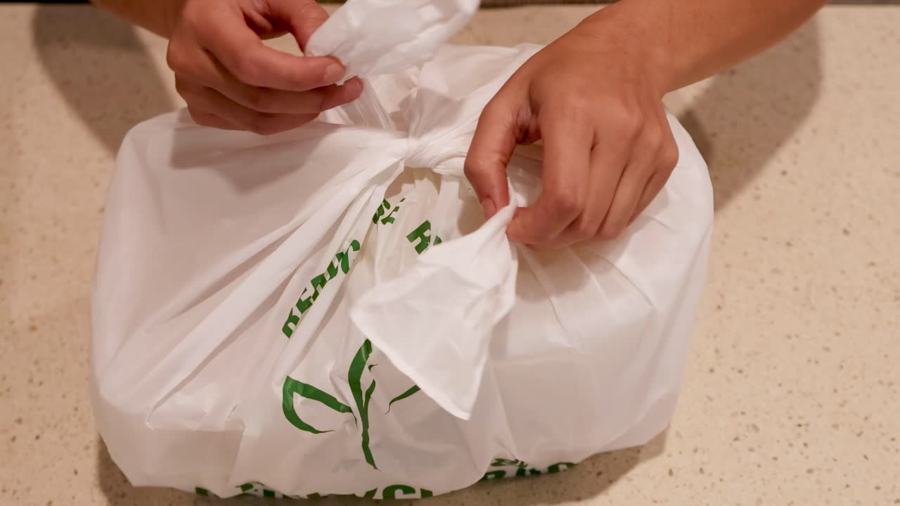Hands carefully open a recyclable bag, revealing a container inside on a kitchen countertop.